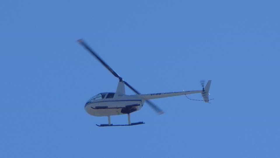 A Robinson R44 helicopter flying against a clear blue sky