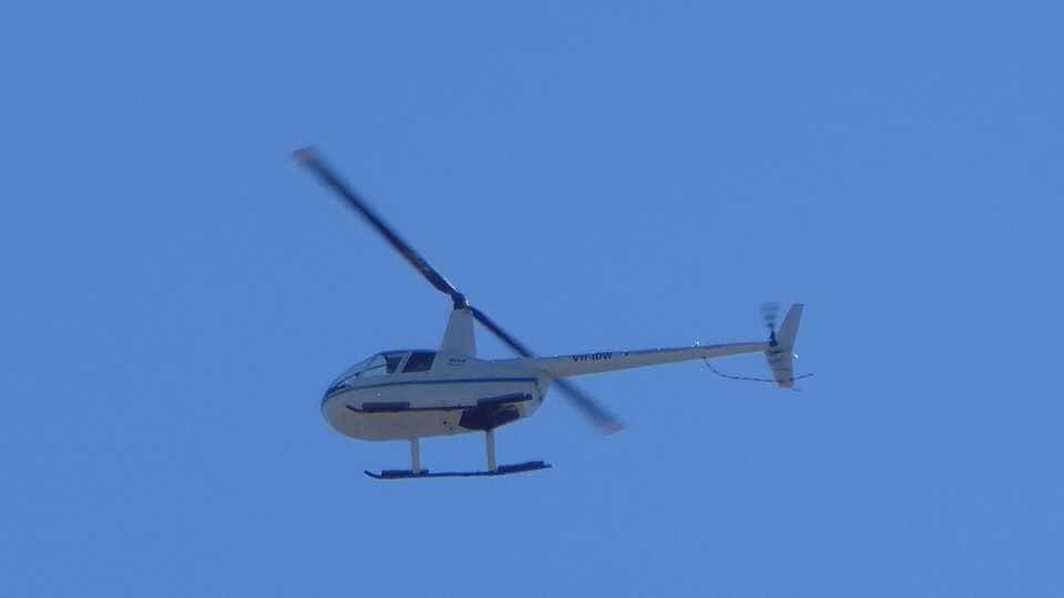 A Robinson R44 helicopter flying against a clear blue sky over Perth