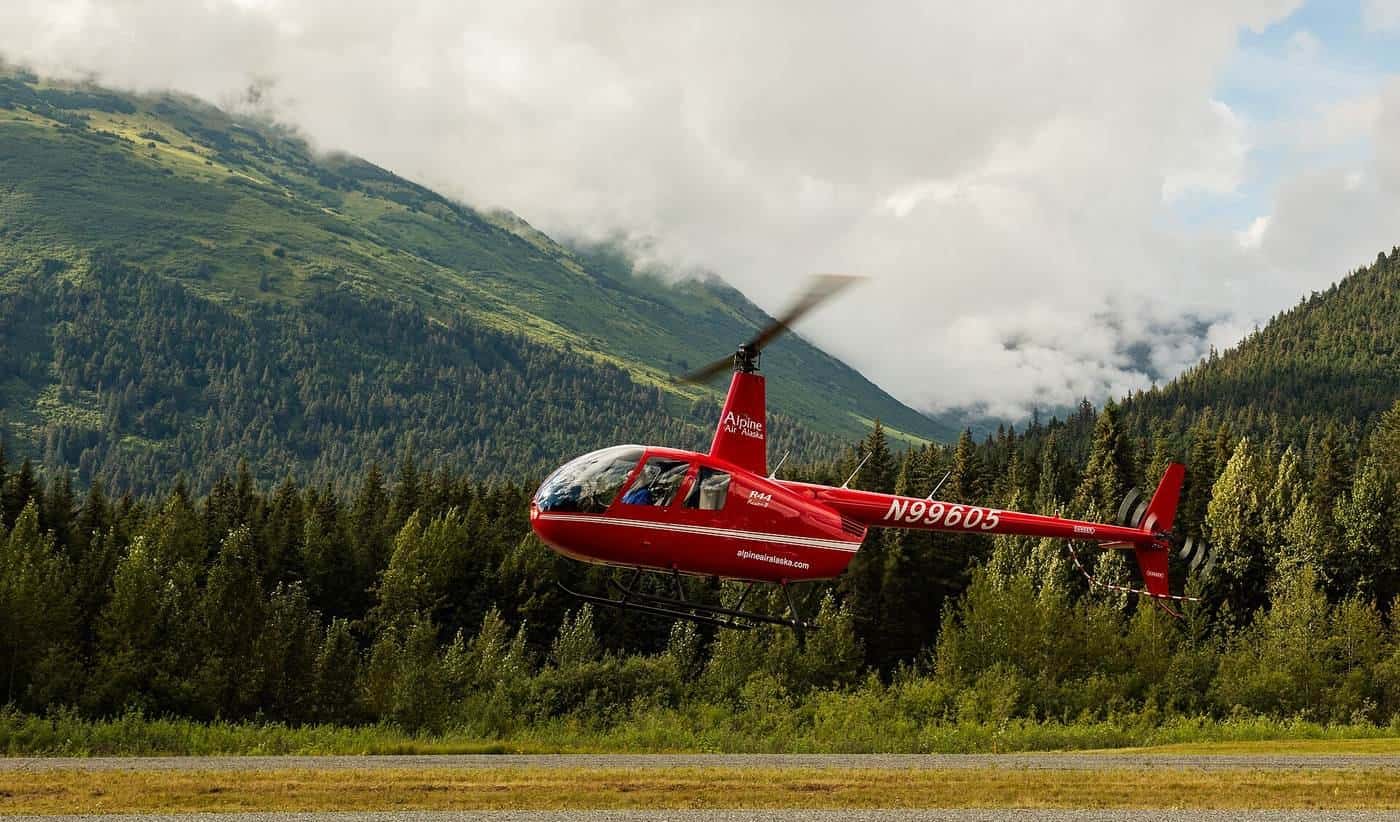 A red helicopter lifting off near forest