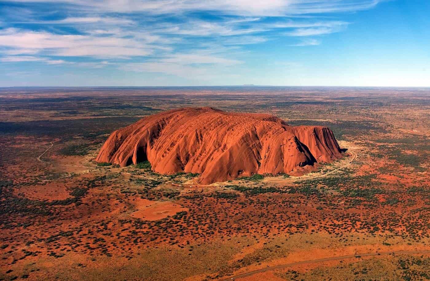 Uluru seen from a helicopter rising above red desert country